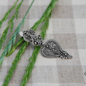 May include: A silver filigree heart pendant with intricate details. The pendant is hanging from a silver chain.