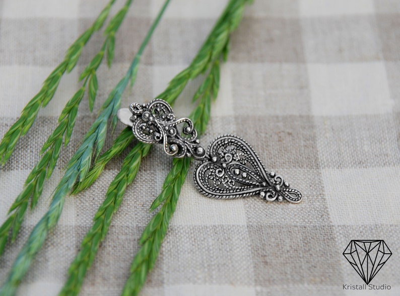 May include: A silver filigree heart pendant with intricate details. The pendant is hanging from a silver chain.