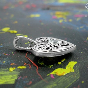May include: A silver heart-shaped pendant with an intricate filigree design and a clear gemstone in the center.