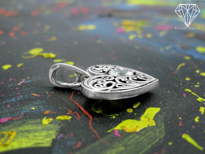 May include: A silver heart-shaped pendant with an intricate filigree design and a clear gemstone in the center.