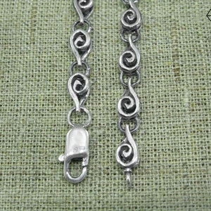 May include: Silver chain bracelet with a clasp closure. The chain is made of a series of connected silver swirls.