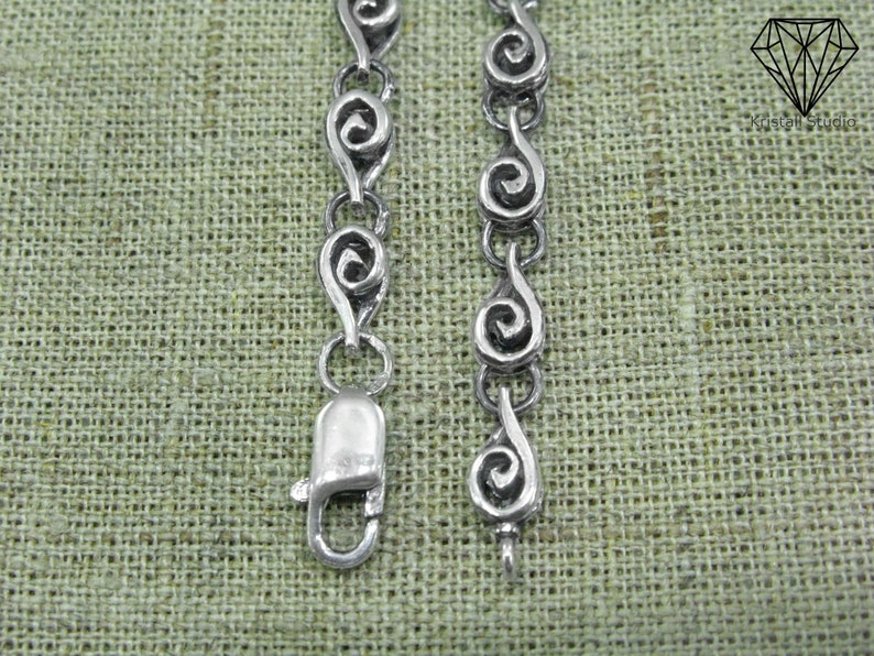 May include: Silver chain bracelet with a clasp closure. The chain is made of a series of connected silver swirls.