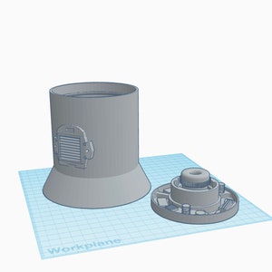 Puede incluir: Un objeto cilíndrico gris con una base ensanchada y un detalle de ventilación rectangular. Al lado, un componente circular con una parte central elevada y detalles circundantes. Los objetos están sobre una cuadrícula azul.