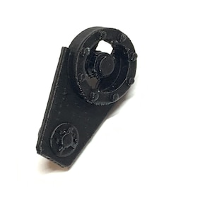 May include: Black plastic gear with a round, toothed wheel and a small, round knob. The gear is attached to a flat, rectangular piece of plastic.