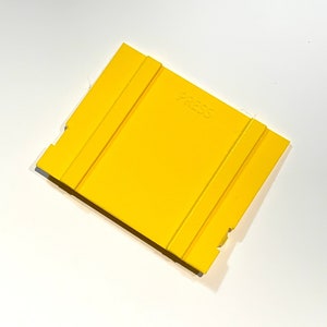 May include: A yellow plastic press plate with the word "PRESS" embossed on the surface.