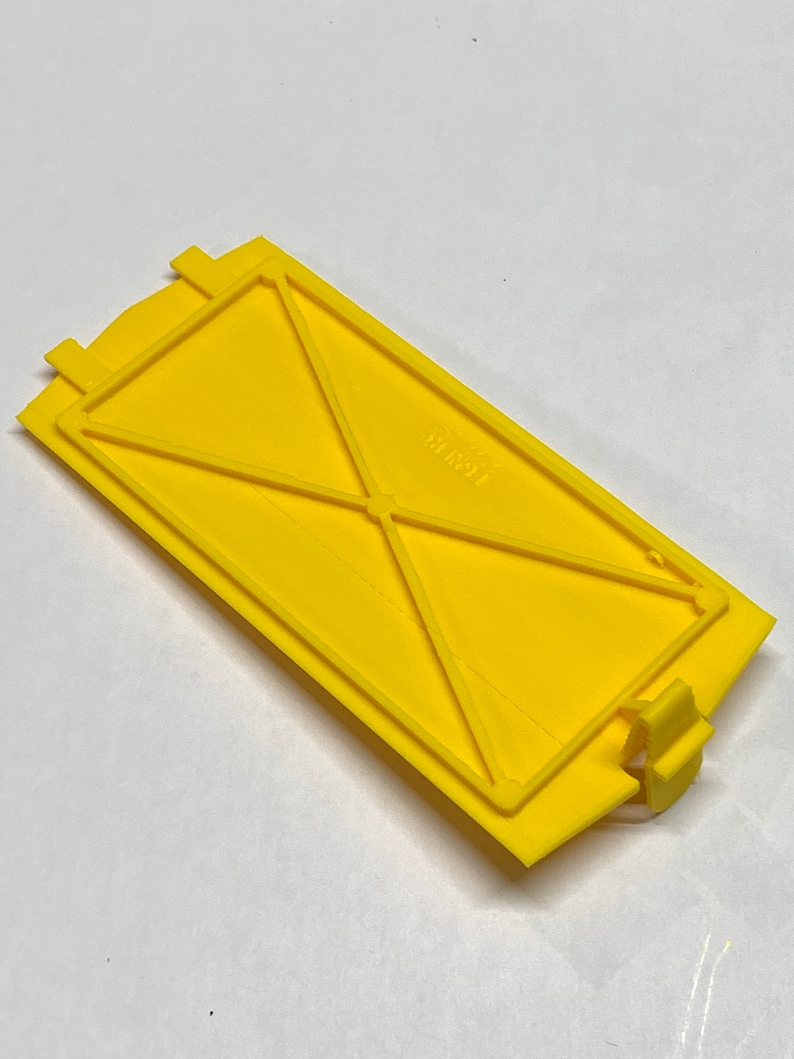 May include: A yellow plastic cover with a rectangular shape and a series of internal ridges. The cover has a small tab on the right side and the text "1991" is visible on the surface.