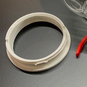 May include: White plastic ring with a smooth, rounded surface. The ring has a raised lip on the outer edge.