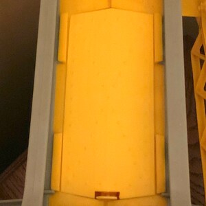 May include: A yellow toy truck bed with a gray metal frame. The bed is empty and has a small opening at the bottom.