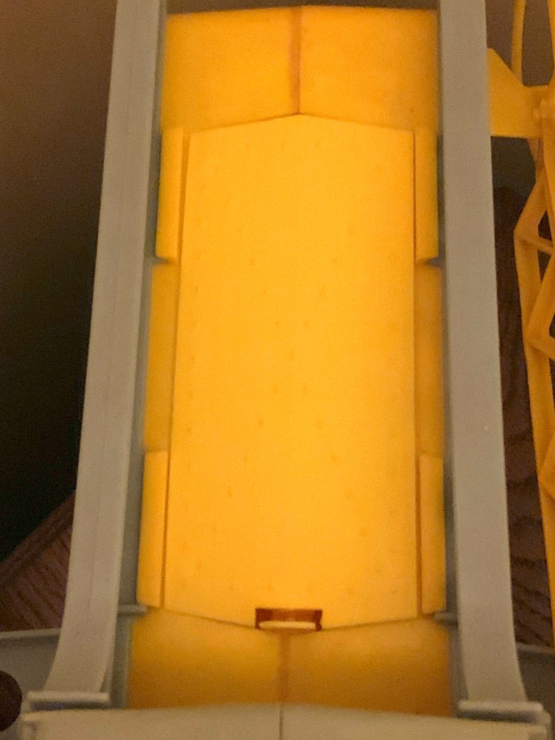 May include: A yellow toy truck bed with a gray metal frame. The bed is empty and has a small opening at the bottom.