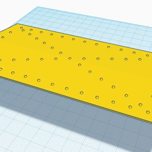 May include: A yellow plastic base with a rectangular shape and multiple holes. The base has a slight curve on one side and a small, rectangular cutout on the other side.