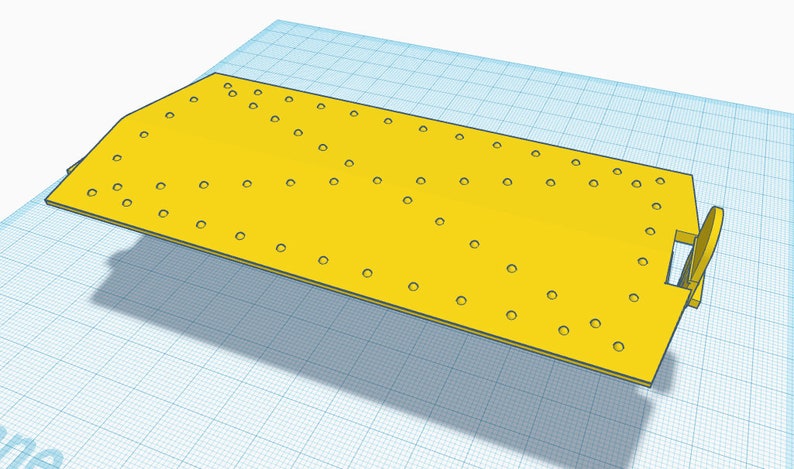 May include: A yellow plastic base with a rectangular shape and multiple holes. The base has a slight curve on one side and a small, rectangular cutout on the other side.