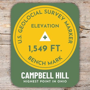 Può includere: Un adesivo rotondo verde e giallo con il testo "U.S. Geological Survey Marker" e "Elevation 1,549 FT. Bench Mark". L'adesivo ha anche il testo "Campbell Hill Highest Point in Ohio".