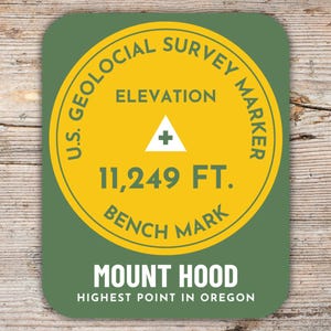 Könnte beinhalten: Ein runder Aufkleber in Grün und Gelb mit dem Text "U.S. Geological Survey Marker" und "Elevation 11,249 FT. Bench Mark". Der Aufkleber trägt außerdem den Text "Mount Hood Highest Point in Oregon".