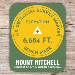Könnte beinhalten: Ein runder Aufkleber in Grün und Gelb mit dem Text "U.S. GEOLOCIAL SURVEY MARKER" und "ELEVATION 6,684 FT. BENCH MARK". Der Aufkleber trägt außerdem den Text "MOUNT MITCHELL HIGHEST POINT IN NORTH CAROLINA".