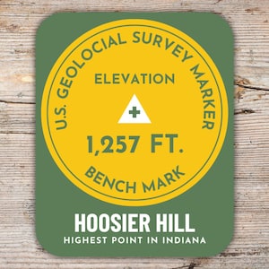 May include: A green and yellow square sticker with the text "U.S. GEOLOGICAL SURVEY MARKER" and "ELEVATION 1,257 FT. BENCH MARK". The sticker reads "HOOSIER HILL HIGHEST POINT IN INDIANA".