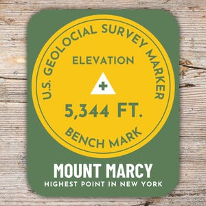 Könnte beinhalten: Ein runder Aufkleber in Grün und Gelb mit dem Text "U.S. Geological Survey Marker" und "Elevation 5,344 FT. Bench Mark". Der Aufkleber trägt außerdem den Text "Mount Marcy Highest Point in New York".