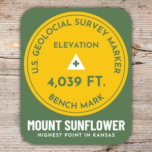 Könnte beinhalten: Ein runder Aufkleber in Grün und Gelb mit dem Text "U.S. Geological Survey Marker" und "Elevation 4,039 FT. Bench Mark" in einem Kreis. Der Text "Mount Sunflower Highest Point in Kansas" befindet sich unter dem Kreis.