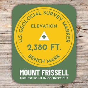 Può includere: Un adesivo rotondo verde e giallo con il testo "U.S. Geological Survey Marker" e "Elevation 2,380 FT. Bench Mark". L'adesivo ha anche il testo "Mount Frissell Highest Point in Connecticut".