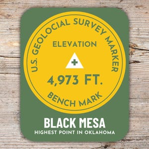 Könnte beinhalten: Ein runder Aufkleber in Grün und Gelb mit dem Text "U.S. Geological Survey Marker" und "Elevation 4,973 FT. Bench Mark". Der Aufkleber trägt außerdem den Text "Black Mesa Highest Point in Oklahoma".