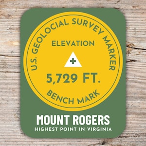 Könnte beinhalten: Ein runder Aufkleber in Grün und Gelb mit dem Text "U.S. Geological Survey Marker" und "Elevation 5,729 FT. Bench Mark". Der Aufkleber trägt außerdem den Text "Mount Rogers Highest Point in Virginia".
