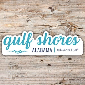 May include: A blue and white sticker with the text "gulf shores ALABAMA | N 30.25°, W 87.70°" and a wavy line graphic.