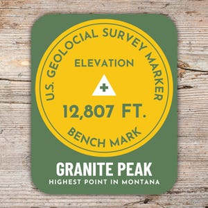 Könnte beinhalten: Ein runder Aufkleber in Grün und Gelb mit dem Text "U.S. Geological Survey Marker" und "Elevation 12,807 FT. Bench Mark". Der Aufkleber trägt außerdem den Text "Granite Peak Highest Point in Montana".