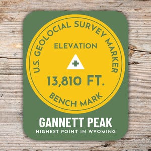 Könnte beinhalten: Ein runder Aufkleber in Grün und Gelb mit dem Text "U.S. Geological Survey Marker" und "Elevation 13,810 FT. Bench Mark". Der Aufkleber trägt außerdem den Text "Gannett Peak Highest Point in Wyoming".