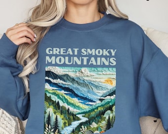 Könnte beinhalten: Ein blaues Sweatshirt mit einem Aufdruck des Great Smoky Mountains National Park. Der Aufdruck zeigt eine farbenfrohe Illustration von Bergen, Bäumen und einem Fluss.