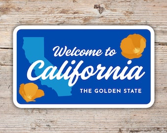 May include: A rectangular sticker with a blue background and white border. The sticker features the text "Welcome to California" and "California" in white script. A light blue outline of California and two orange poppies are also present. The text "THE GOLDEN STATE" is at the bottom.