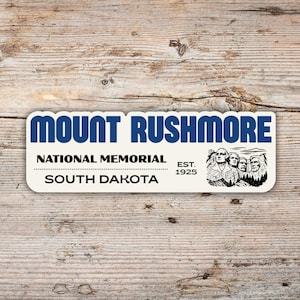Puede incluir: Una pegatina rectangular con el texto MOUNT RUSHMORE en letras azules grandes, seguido de NATIONAL MEMORIAL, EST. 1925 y SOUTH DAKOTA en negro. A la derecha hay una ilustración en blanco y negro de los cuatro rostros presidenciales.