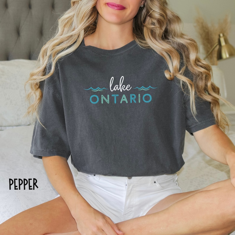 May include: A dark gray t-shirt with the text "lake ONTARIO" in blue and white lettering. The text is surrounded by a wavy line design.