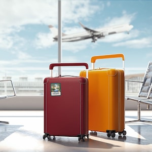 May include: Two suitcases, one red and one yellow, are sitting in an airport terminal. The red suitcase has a sticker that says "Louisiana" on it.