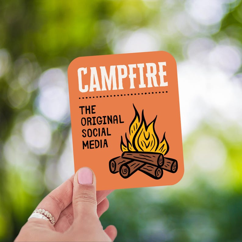 May include: An orange square sticker with the word "CAMPFIRE" in white block letters. Below, the text reads "THE ORIGINAL SOCIAL MEDIA". A graphic of a campfire with flames and logs is featured.