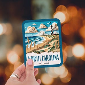 May include: A blue and white sticker with a paper cut-out style illustration of a lighthouse on a beach with the text "North Carolina Est. 1789".