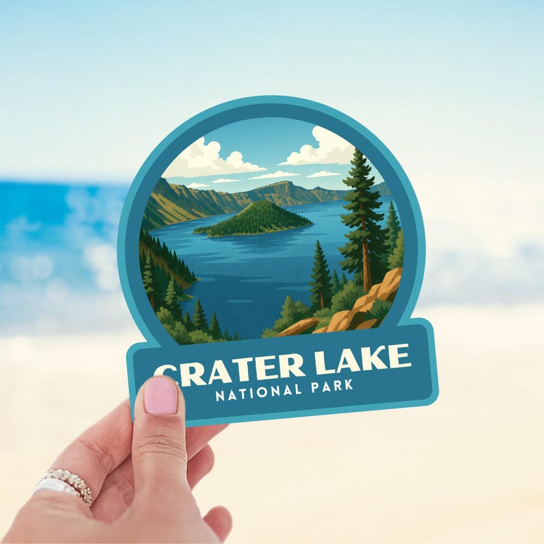 May include: A sticker featuring a scenic illustration of Crater Lake National Park. The design includes a blue lake, green island, and surrounding mountains, with the text "CRATER LAKE NATIONAL PARK" in white.