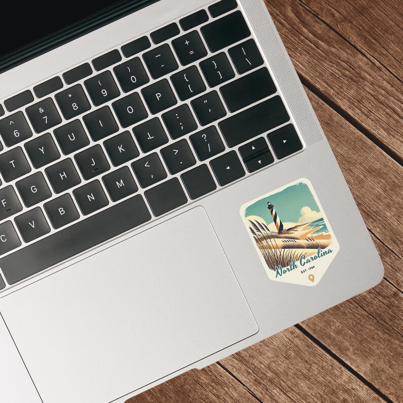 May include: A vintage-style sticker featuring a lighthouse on a sandy beach with the text "North Carolina Est. 1799".