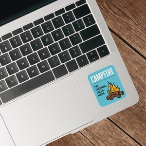 May include: A blue sticker on a laptop with the word "CAMPFIRE" at the top and "THE ORIGINAL SOCIAL MEDIA" below. A cartoon campfire with flames and logs is also on the sticker.
