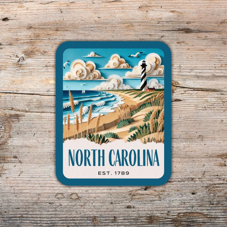 May include: A blue and white illustrated postcard featuring a lighthouse on a sandy beach with waves crashing on the shore. The text "NORTH CAROLINA EST. 1789" is printed on the postcard.