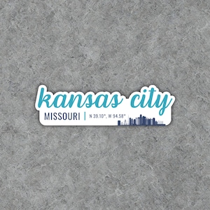 Puede incluir: Una pegatina azul y blanca con el texto "kansas city" y "MISSOURI | N 39.10&deg;, W 94.58&deg;". Un horizonte estilizado de la ciudad se encuentra debajo del texto.
