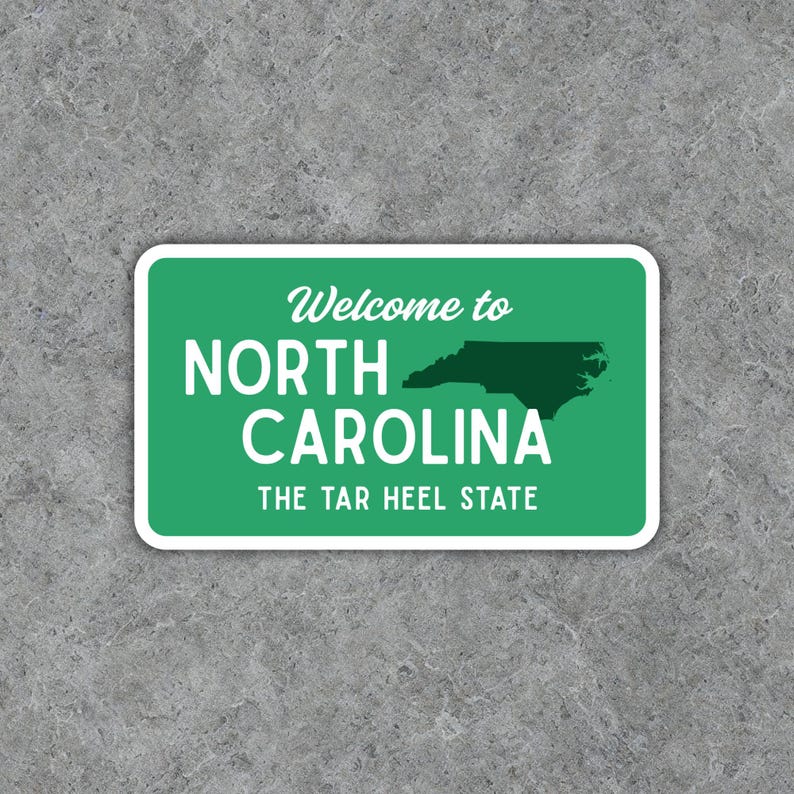 Puede incluir: Una pegatina rectangular con fondo verde y borde blanco. El texto "Welcome to NORTH CAROLINA" se muestra en blanco, con un contorno verde oscuro del estado y el texto "THE TAR HEEL STATE" debajo.