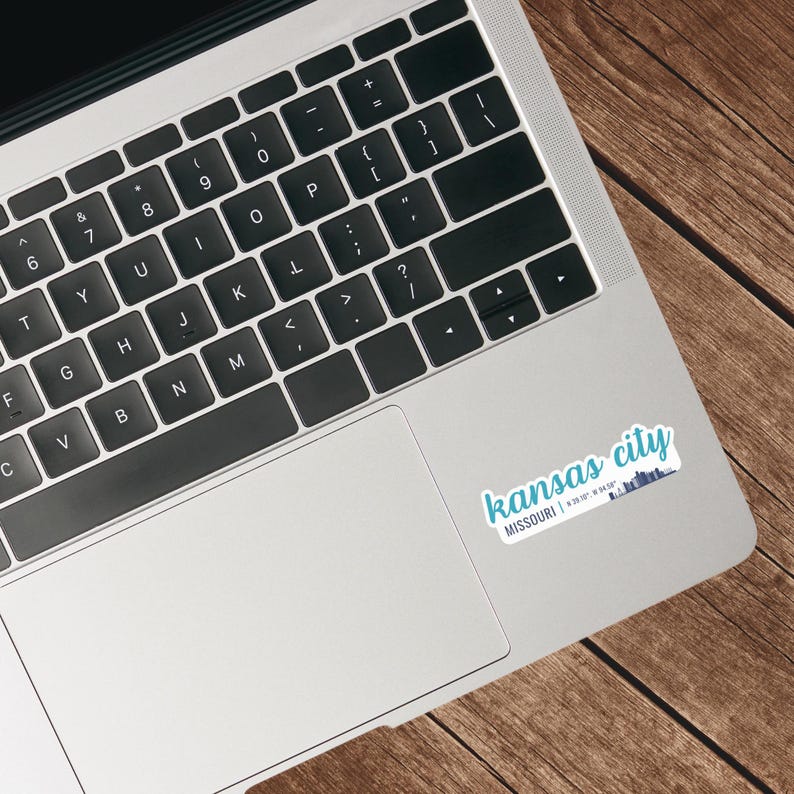 Puede incluir: Un ordenador port&aacute;til con una pegatina en el lado derecho del trackpad. La pegatina es blanca con texto azul que dice "kansas city MISSOURI | 39.0997&deg; N, 94.5786&deg; W".