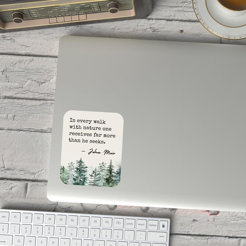 May include: A white laptop sticker with a watercolor illustration of a forest and a quote by John Muir: "In every walk with nature one receives far more than he seeks."