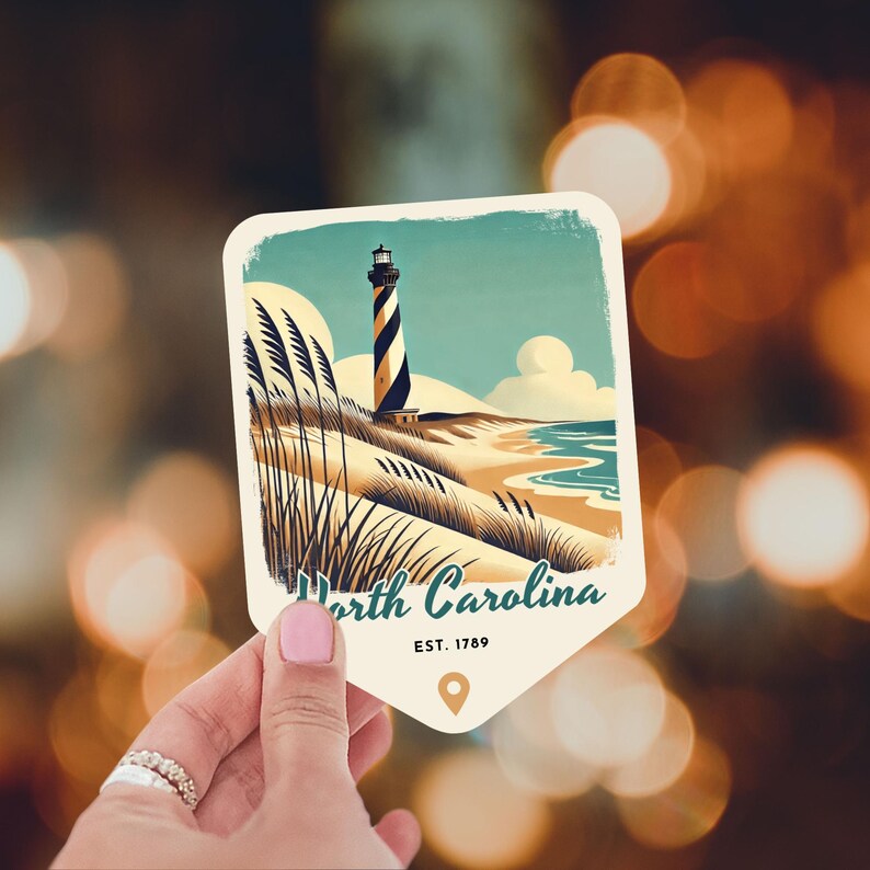 May include: A vintage-style illustration of a lighthouse on a sandy beach with green grass and blue water. The text "North Carolina EST. 1789" is below the image.