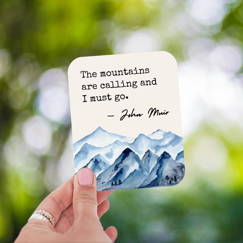 K&ouml;nnte beinhalten: Eine wei&szlig;e Karte mit einer blauen Aquarell-Berglandschaft. Die Karte zeigt das Zitat "The mountains are calling and I must go." - John Muir.