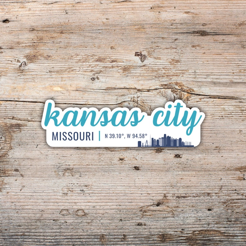 Puede incluir: Una pegatina blanca con una gr&aacute;fica de horizonte de Kansas City, Missouri, en azul y blanco. El texto "kansas city" est&aacute; en azul y el texto "MISSOURI | N 39.10&deg;, W 94.58&deg;" est&aacute; en negro.