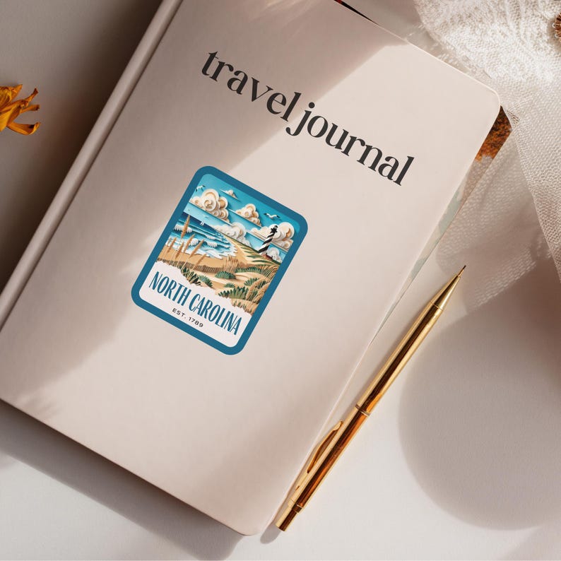 May include: A travel journal with a sticker on the front. The sticker is blue and white and features a beach scene with the text "North Carolina Est. 1789".