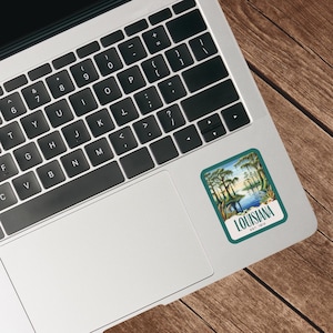 May include: A vintage-style sticker with a green border and a scene of a swamp with cypress trees and water. The text "LOUISIANA EST. 1812" is printed in white on a blue banner at the bottom of the sticker.
