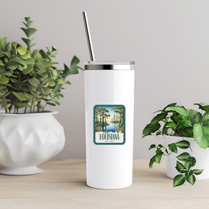 May include: White stainless steel tumbler with a green and blue sticker featuring a scenic view of a Louisiana bayou with the text "Louisiana Est. 1912".