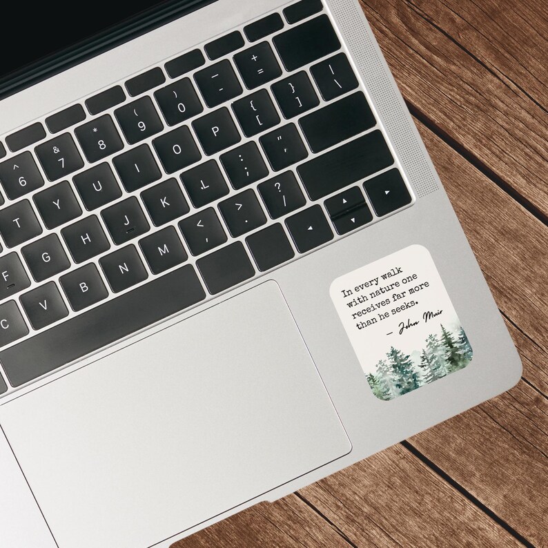 May include: A laptop computer with a sticker on the right side. The sticker features a watercolor illustration of a forest with the quote "In every walk with nature one receives far more than he seeks." - John Muir.