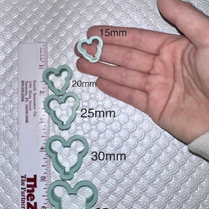 May include: Five different sized plastic cookie cutters in the shape of a cartoon mouse head. The cutters are light blue and are arranged in a row from smallest to largest. The cutters are measured in millimetres: 15mm, 20mm, 25mm, 30mm, and 35mm.